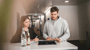 Dos estudiants en pràctiques estan drets a una taula mirant una tauleta.